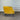 Yellow armchair with black legs against a corrugated metal wall.