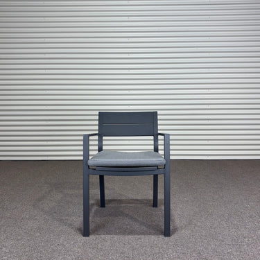 Gray chair with cushion against a corrugated metal wall.