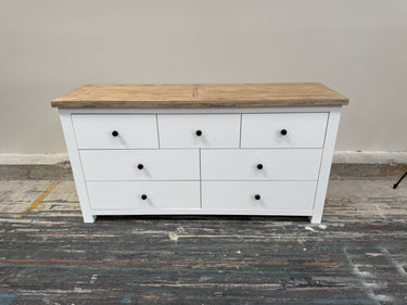 White dresser with wooden top on a gray floor against a beige wall