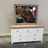White dresser with wooden top and mirror reflecting a store interior.