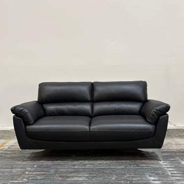 Black leather sofa on a wooden floor with a plain wall background