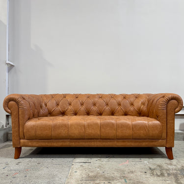 Brown leather sofa in a room with a plain wall.