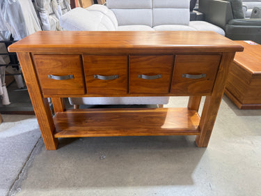 A medium brown wooden console table with four drawers, metal handles, and a lower shelf, photographed in a furniture store setting.