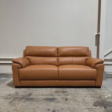 Brown leather sofa in a room with a plain wall and concrete floor.