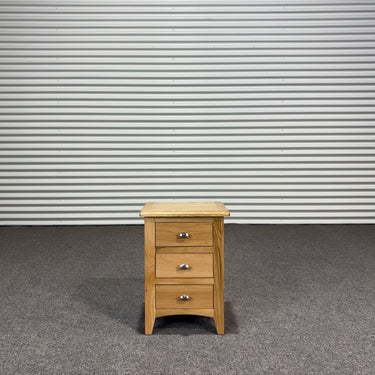 Wooden nightstand with three drawers against a corrugated metal wall.