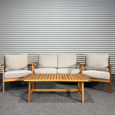 Outdoor furniture set with wooden table and beige cushions against a corrugated metal wall.