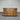 Wooden dresser with multiple drawers against a corrugated metal wall.