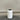 White cylindrical trash can with black lid on a wooden floor against a plain wall.