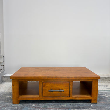 Wooden coffee table with a drawer on a gray floor against a white wall