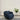 Blue armchair in a room with a plant on a stand against a plain wall.