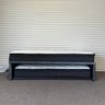 Black metal bed frame with mattresses against a corrugated metal wall.