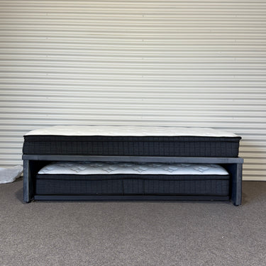 Black metal bed frame with mattresses against a corrugated metal wall.