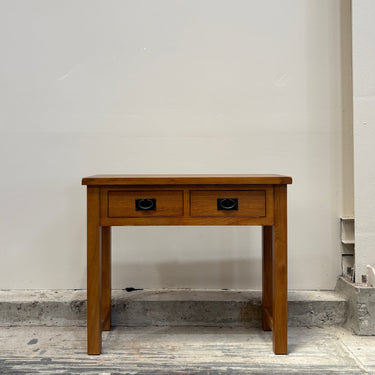 Wooden console table with two drawers against a plain wall.