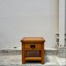 Wooden side table with a drawer against a plain wall.
