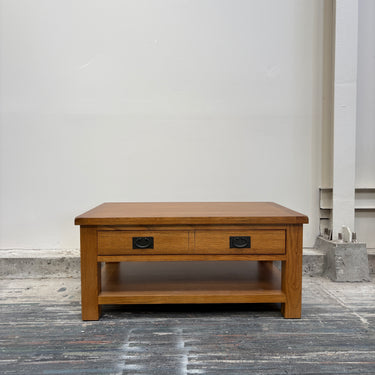 Wooden coffee table with two drawers on a gray floor against a white wall.
