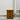 Wooden nightstand with three drawers against a plain wall.