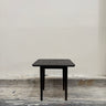 Black square table against a plain white wall.