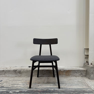 Black chair with gray cushion on a concrete floor against a white wall.