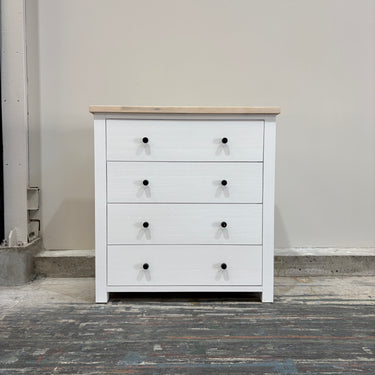 White dresser with black knobs on a wooden floor against a gray wall