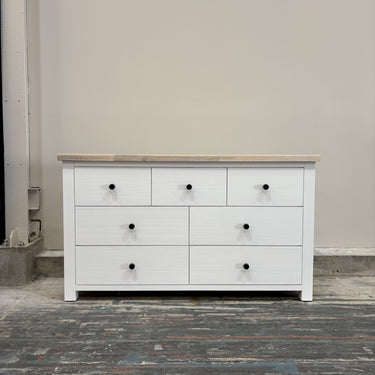 White dresser with black knobs on a gray floor against a plain wall