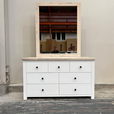 White dresser with a mirror on top in a warehouse setting