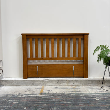 Wooden headboard against a white wall with a plant on the right side.