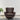 Brown leather armchair with tufted backrest on a wooden floor with a plant in the background.