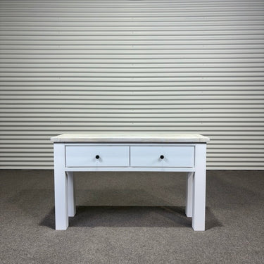 White wooden console table with two drawers against a corrugated metal wall.