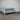 Modern outdoor sofa with gray cushions on a white metal frame against a corrugated metal wall.