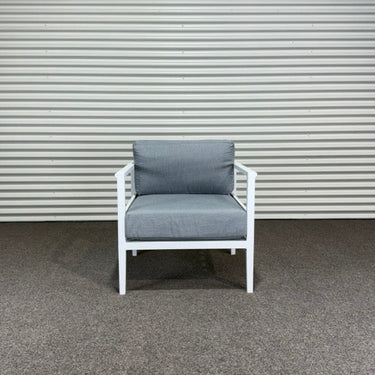 Chair with gray cushions on a concrete floor against a corrugated metal wall.