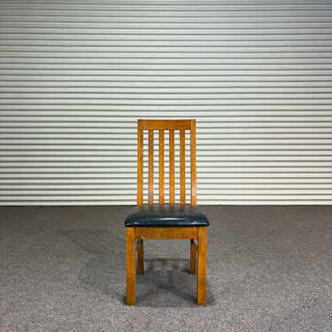 Wooden chair with a black seat against a corrugated metal wall - Wanaka Collection.