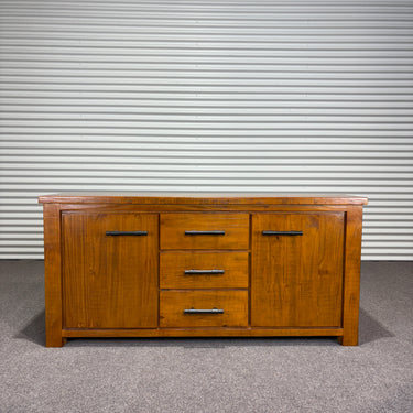 Pine Wood sideboard with drawers and doors with industrial black handles. against a corrugated metal wall.