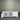 White TV stand with wooden top against a corrugated metal wall.