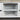 White cabinet with a single shelf and black knobs on a gray carpeted floor.
