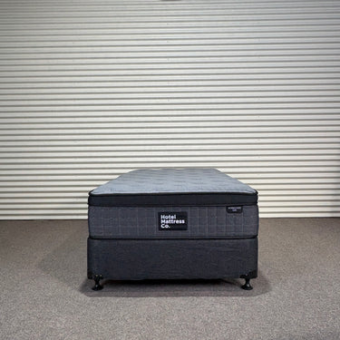 Workhorse LUX king single mattress with matching base, front view showing grey quilted top, dark upholstered base and Hotel Mattress Co label against corrugated wall.