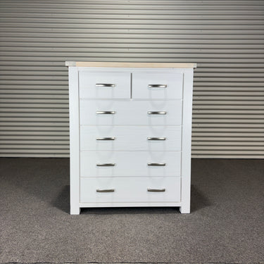 White dresser with multiple drawers against a corrugated metal wall.