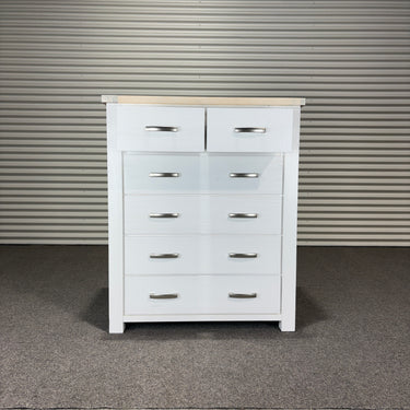 White dresser with multiple drawers against a corrugated metal wall.