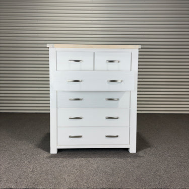 White dresser with multiple drawers against a corrugated metal wall.
