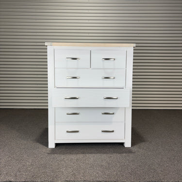 White dresser with multiple drawers against a corrugated metal wall.