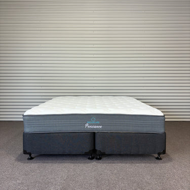 Gray and white mattress with 'Penzance' branding against a striped wall.