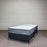 Mattress with 'Chelsea' branding on a gray floor against a corrugated metal wall.