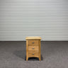 Wooden nightstand with three drawers against a corrugated metal wall.