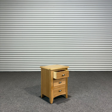 Wooden nightstand with three drawers against a corrugated metal wall.