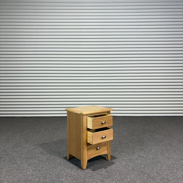 Wooden nightstand with three drawers against a corrugated metal wall.