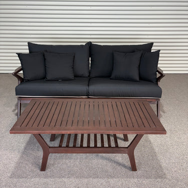Outdoor furniture set with black cushions and a wooden table on a gray floor.