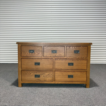 Wooden dresser with multiple drawers against a corrugated metal wall.