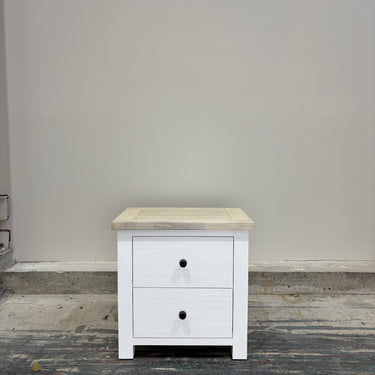 White nightstand with a wooden top against a gray wall.