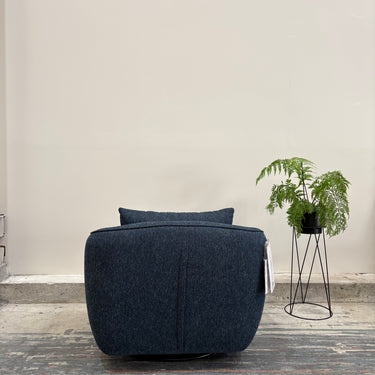 Blue armchair in a minimalistic room with a plant on a stand.
