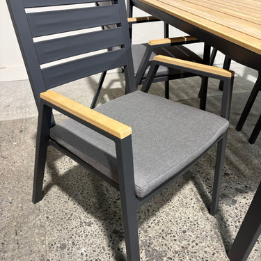 Gray chair with wooden armrests and seat cushion next to a wooden table on a concrete floor.