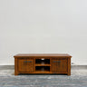 Wooden TV stand with two doors on a wooden floor against a white wall